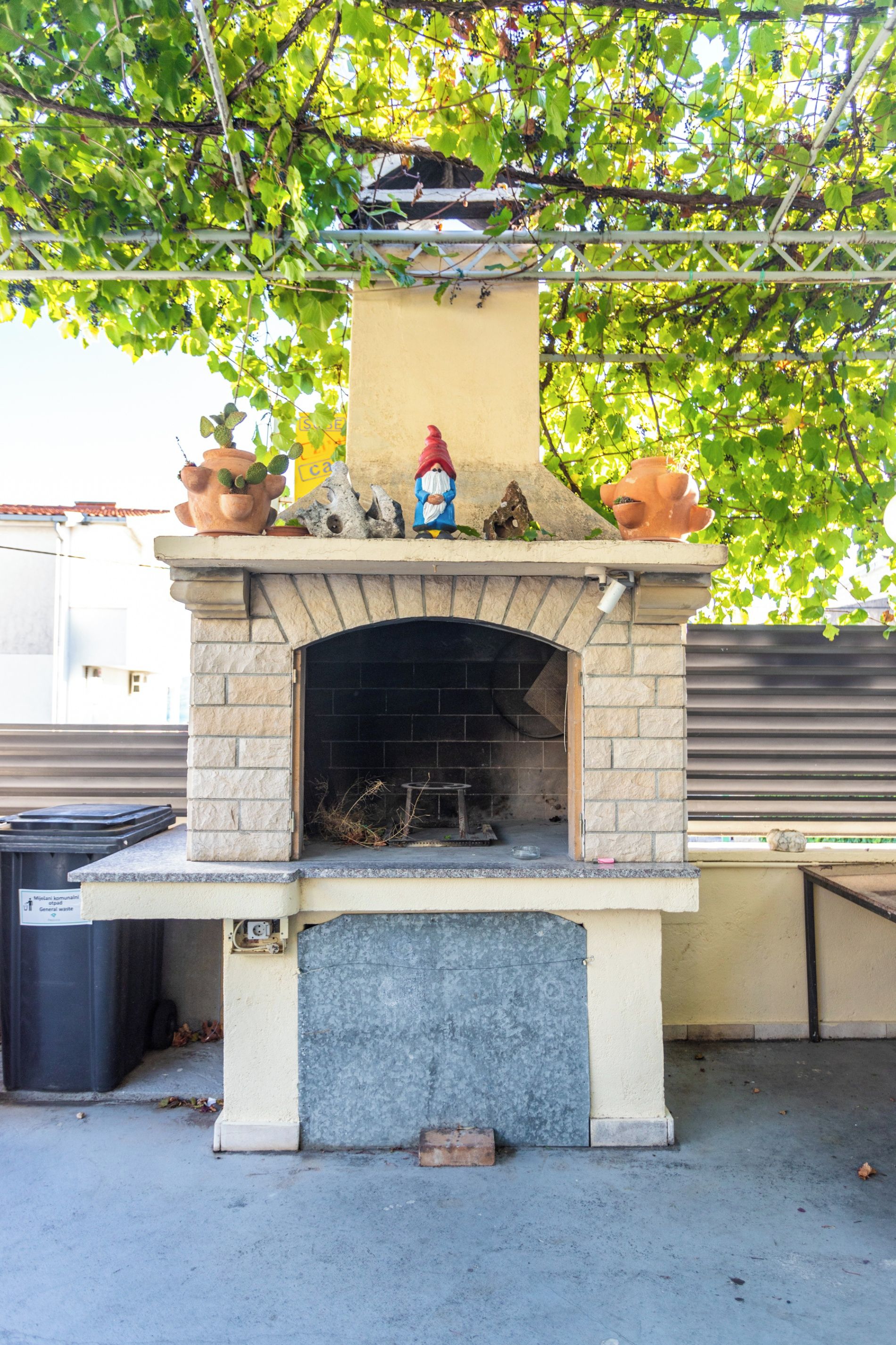 Una chimenea de piedra en el exterior, con una chimenea, rodeada de plantas en macetas y una figura decorativa.