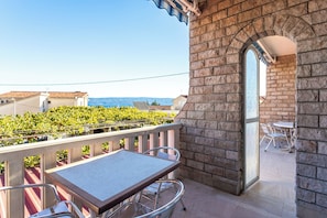 A balcony with a table and chairs, a stone wall, and a view of a vineyard. - A3 - Spacious apt w pool, terrace and sea view (Dugi Rat)
