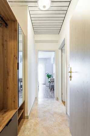 A hallway with a wooden bench, a door with a golden handle, and a tiled floor leading to a room with a plant and a table. - A3 - Spacious apt w pool, terrace and sea view (Dugi Rat)