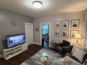 A living room with a flat-screen TV, a sofa, a coffee table, and a lamp. - Close to Brown & RISD lovely 4-bedroom apartment (Providence)