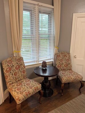 A room with two patterned armchairs, a small round table with a vase, and a window with blinds. - Close to Brown & RISD lovely 4-bedroom apartment (Providence)