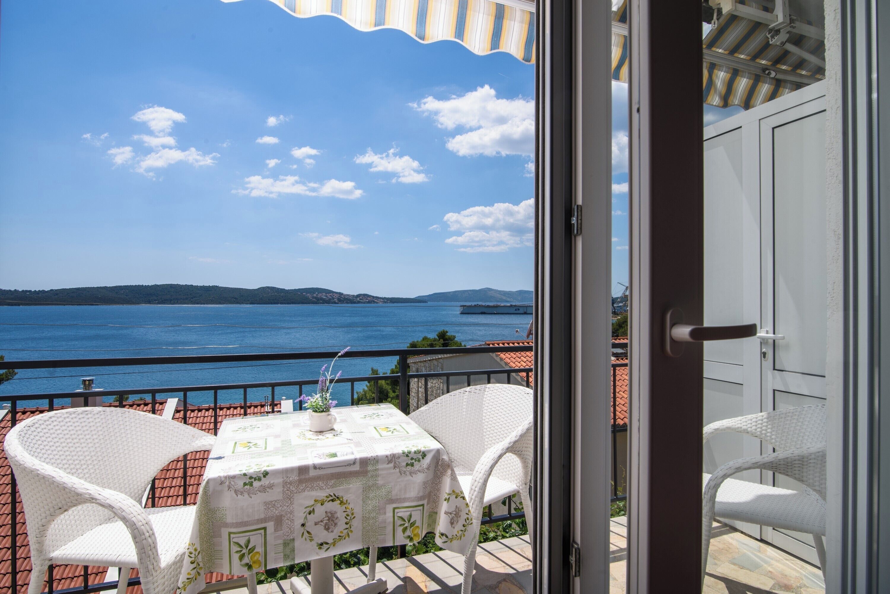 A balcony with a table and chairs, overlooking a body of water and distant hills.