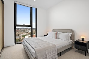 A bedroom with a large window, a bed, a nightstand, and a lamp. - Balcony 3-Bed Apartment Near Albert Park (St Kilda)