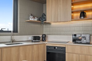 A modern kitchen with wooden cabinets, a built-in oven, a coffee machine, and a Hisense microwave. - Balcony 3-Bed Apartment Near Albert Park (St Kilda)