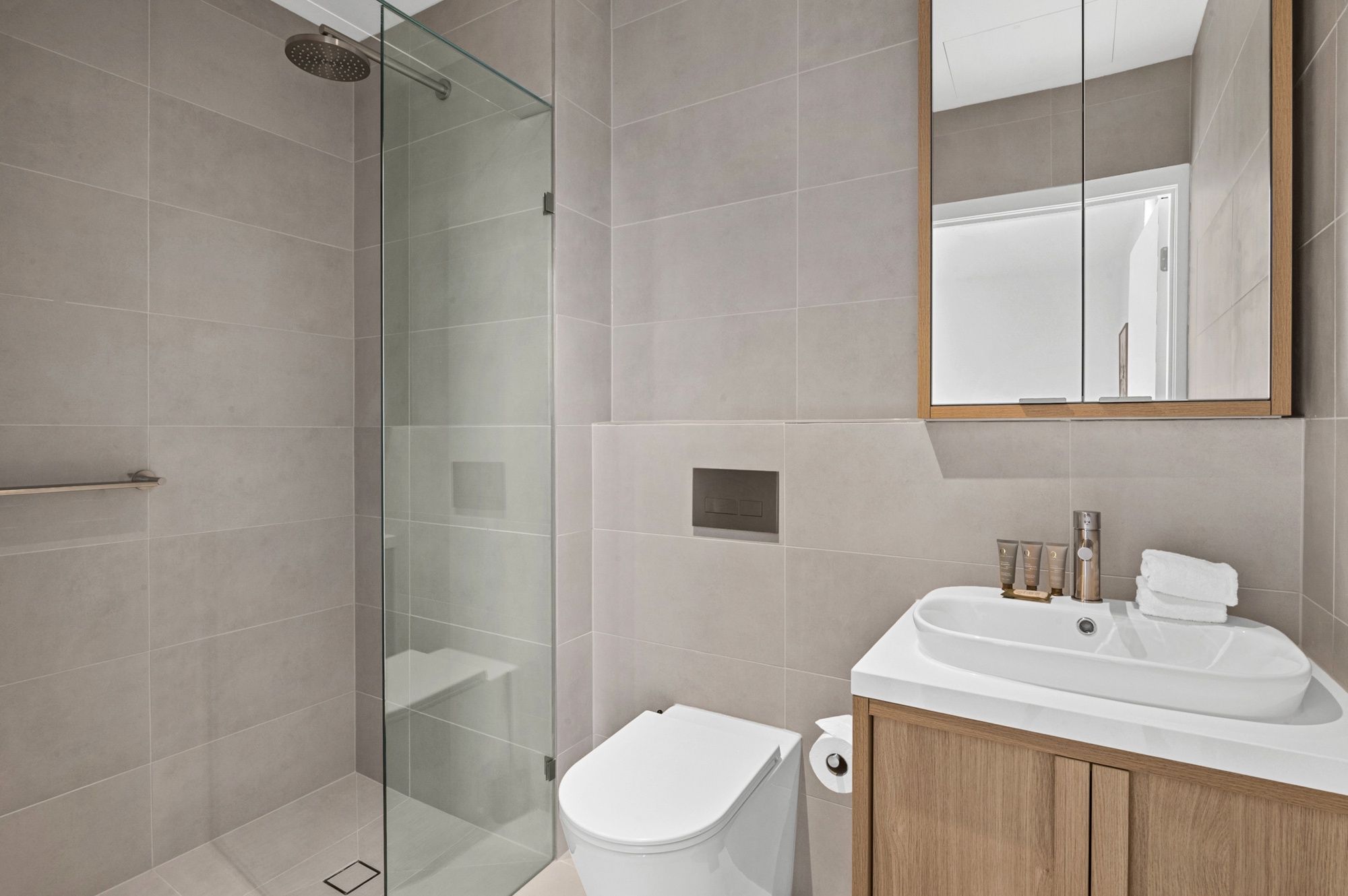 Une salle de bain moderne avec une douche à parois de verre, des toilettes blanches et un meuble-lavabo en bois avec un évier.