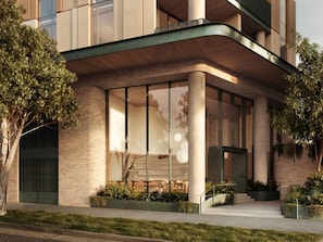 A modern building with large windows, a curved entrance, and a landscaped area with plants. - Balcony 2-Bed Residence Near Albert Park (St Kilda)