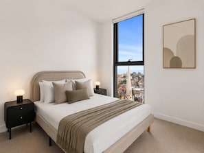 A bedroom with a large window, a bed with multiple pillows, a bedside table with a lamp, and a framed abstract artwork on the wall. - Elevated 3-Bed Residence At Fareham St Kilda (St Kilda)