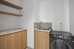 A compact kitchen with a sink, wooden cabinets, and a washing machine. - Light-Filled 3-Bed Brand New Apartment (St Kilda)