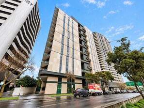 A multi-story building with a modern design, featuring balconies on each floor and a visible commercial sign on the ground level. - Light-Filled 3-Bed Brand New Apartment (St Kilda)