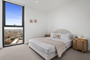 A bedroom with a large window, a bed with a headboard, bedside tables, and a view of a cityscape. - St Kilda Road 2-Bed With Rooftop Access (St Kilda)