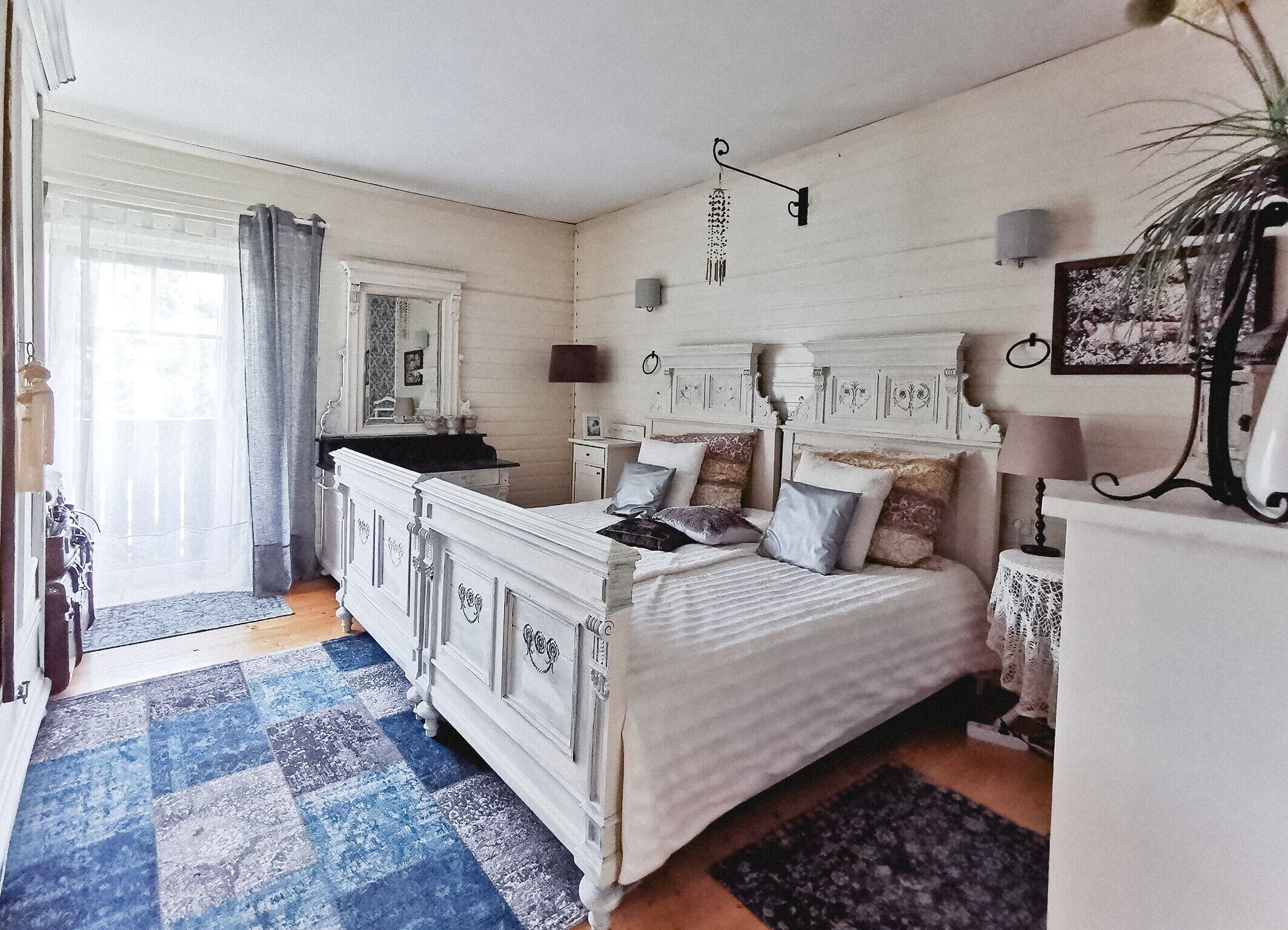 Quarto com uma cama grande, cômoda, espelho e janela com cortinas.