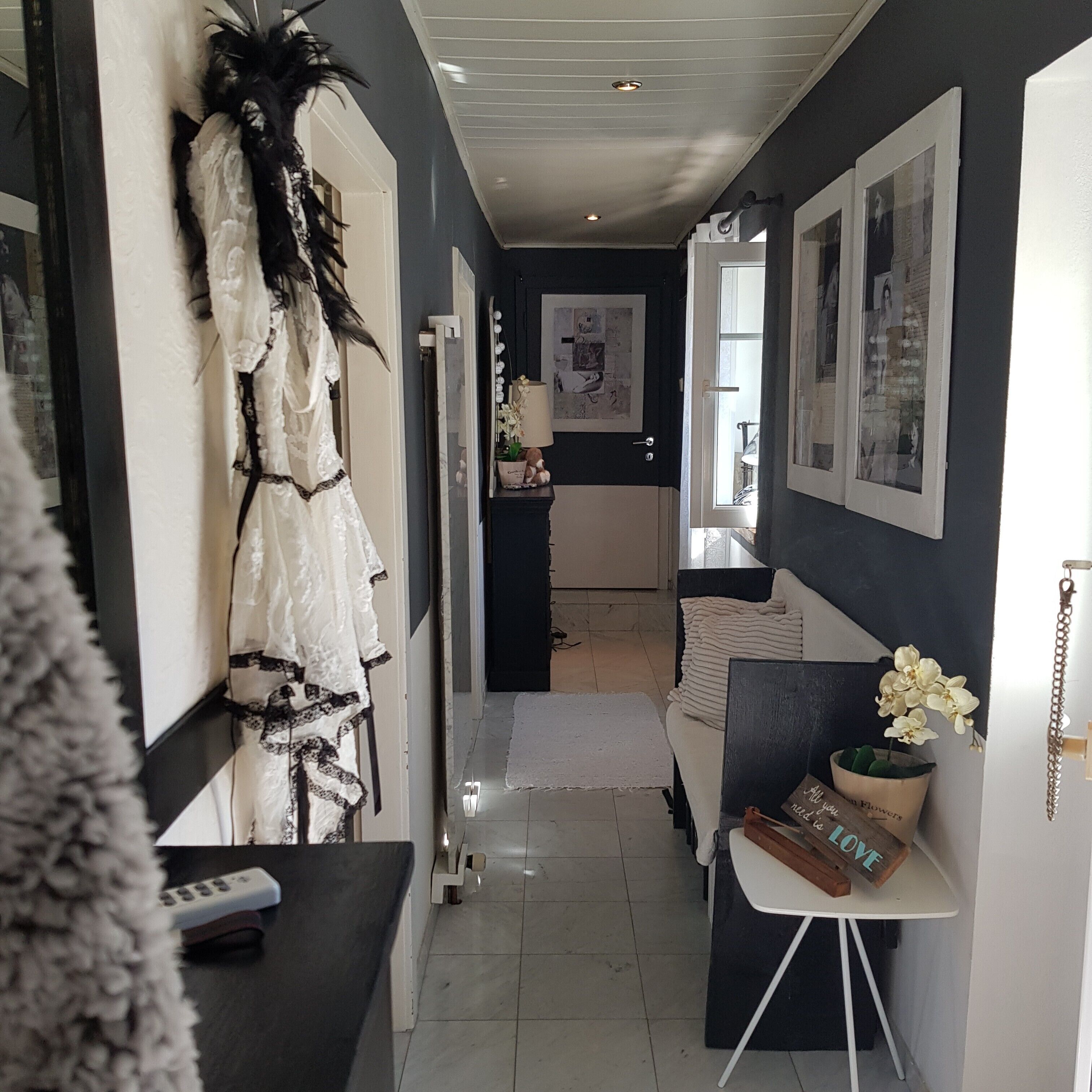 Un couloir avec une porte blanche, un mur orné d’un motif noir et blanc, et une petite table sur laquelle est posé un vase de fleurs.