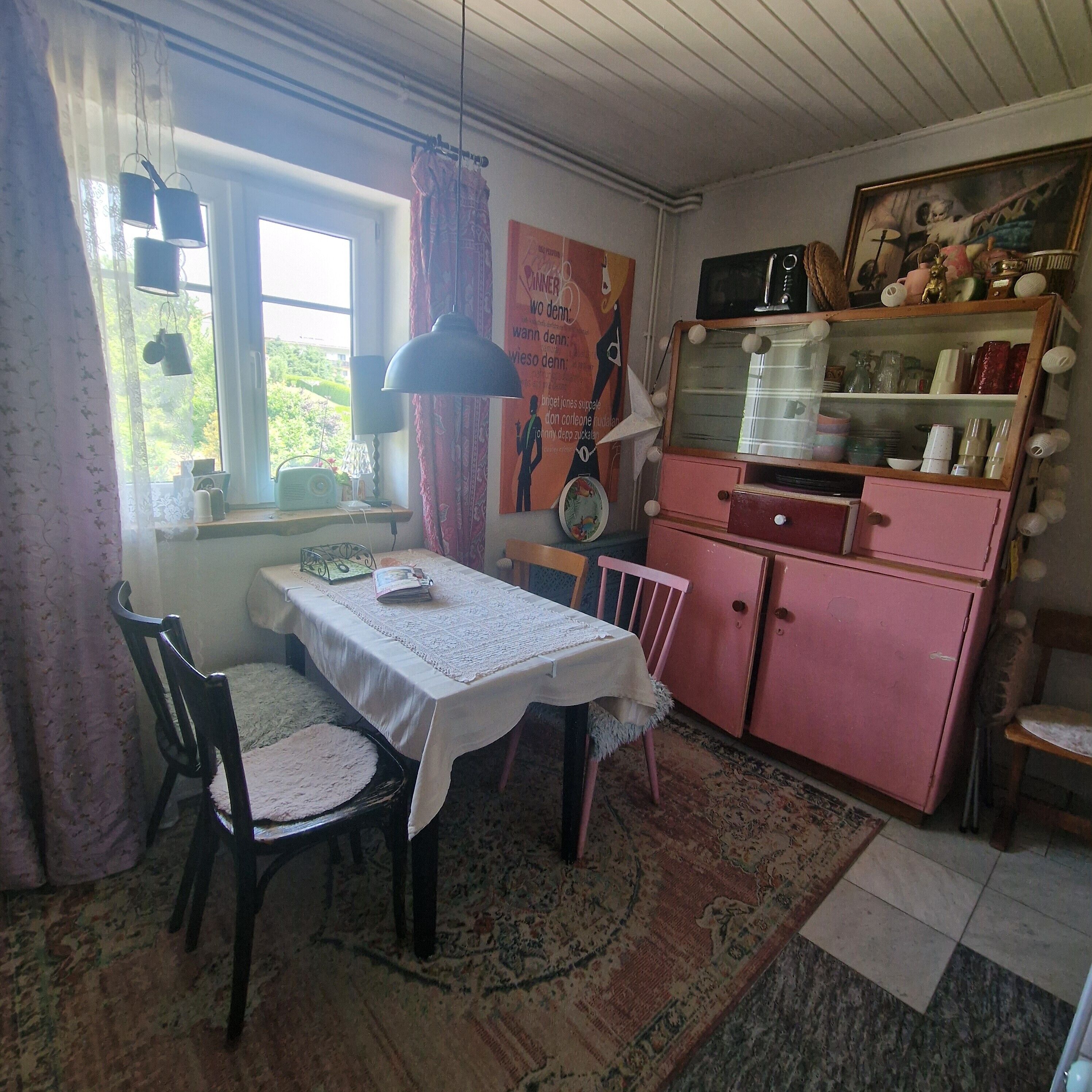 Un comedor con una mesa, sillas, un radio y un refrigerador rosa.