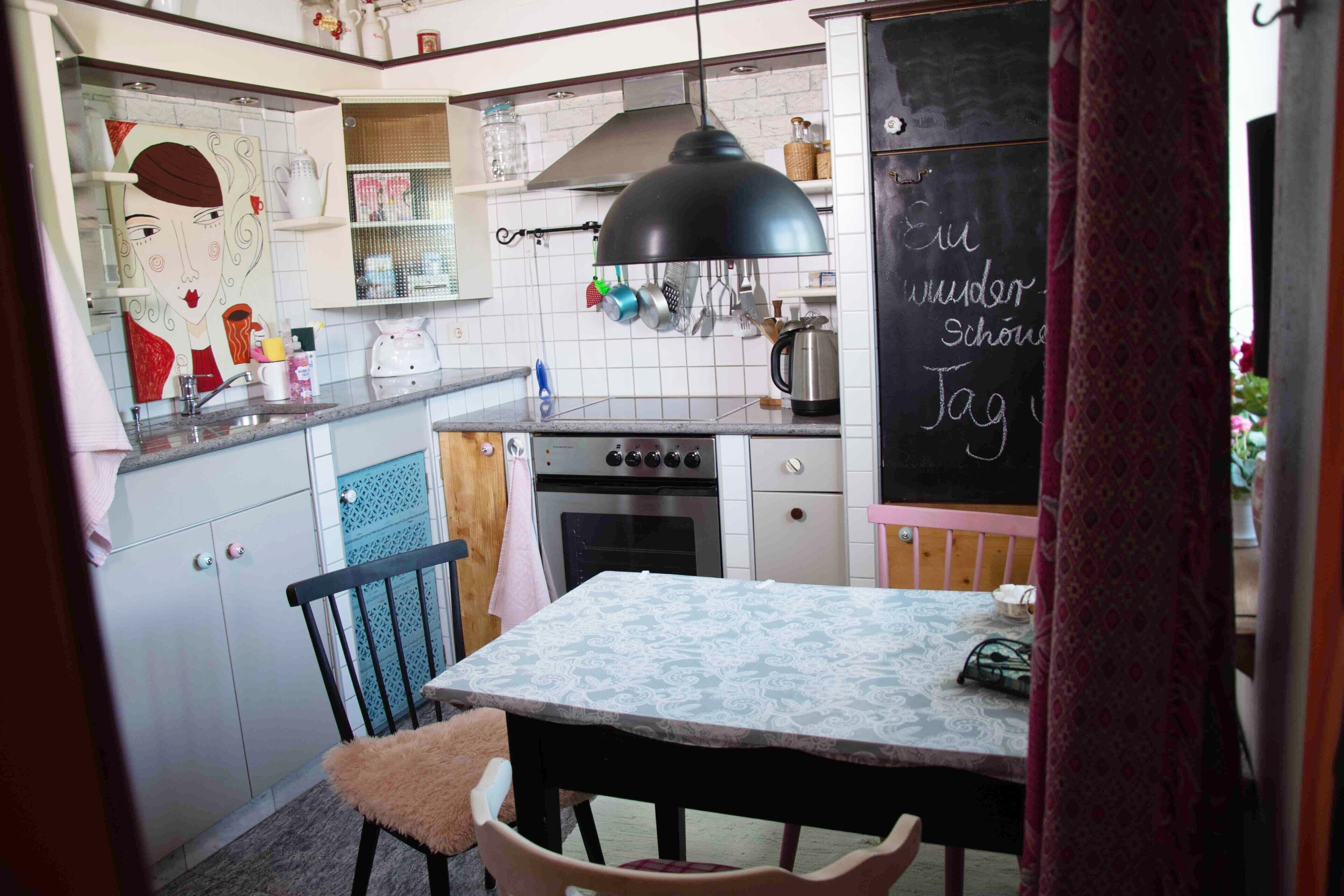 A compact kitchen with a dining area, including a table with a patterned tablecloth, a stove, and various kitchen utensils.
