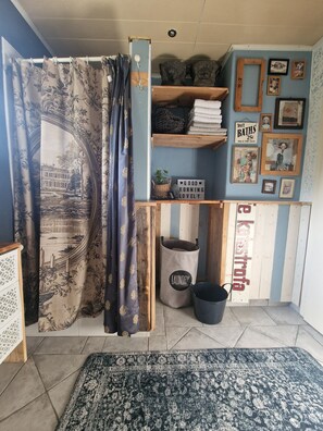 Une pièce avec un rideau représentant un bâtiment historique, une étagère avec des serviettes et un panneau, un panier à linge et un tapis.