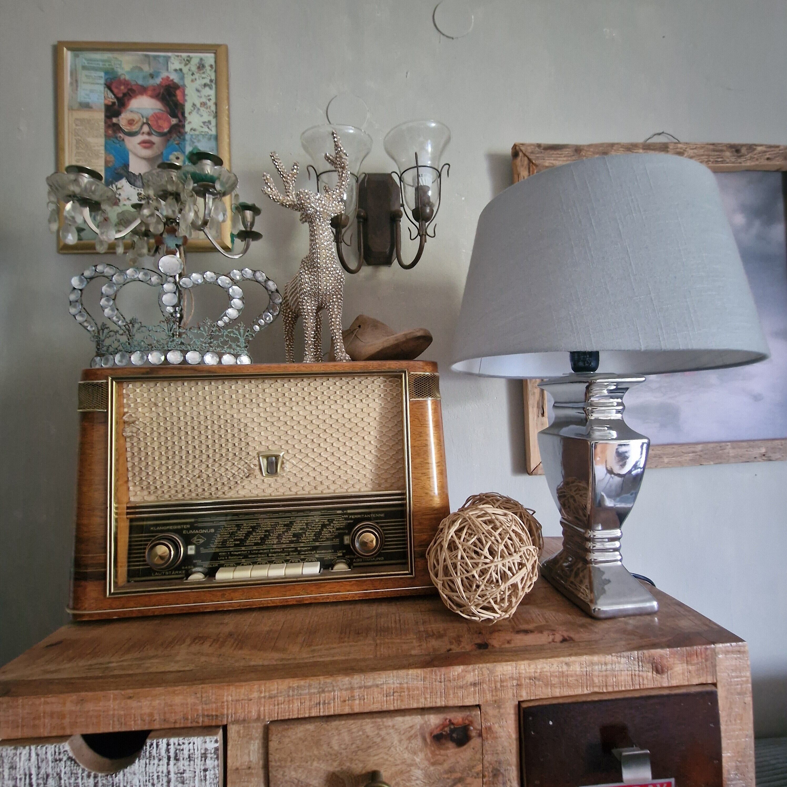 A vintage radio on a wooden cabinet with decorative items, a lamp, and wall sconces.