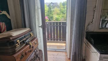 Una habitación con piso de madera, un juego de maletas marrones, un armario blanco y vistas a un balcón con follaje.