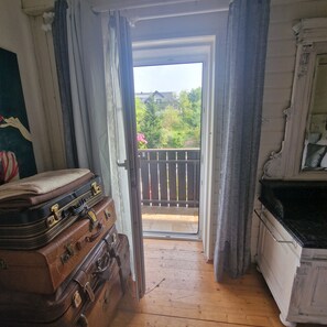 A room with a wooden floor, a set of brown luggage, a white cabinet, and a view of a balcony with greenery outside.