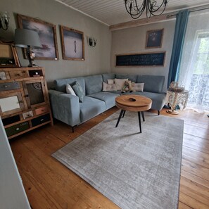 Un salon comprenant un canapé, une table basse, un meuble en bois avec des tiroirs et un lustre.