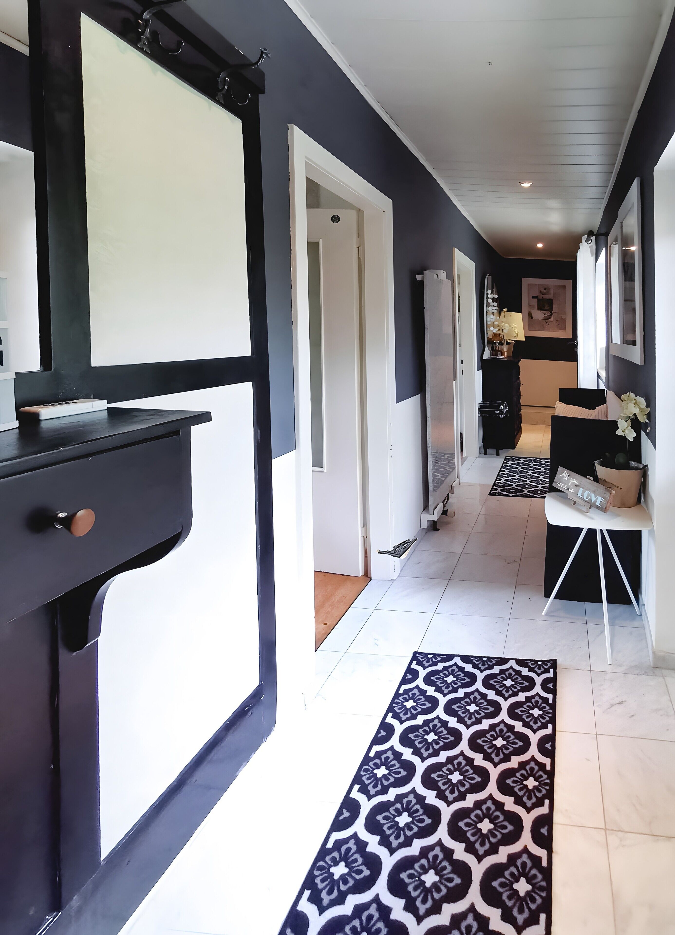Un pasillo con un tapete estampado, una puerta blanco y negro y una pared blanca con un cuadro enmarcado.