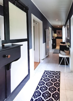 A hallway with a patterned rug, a black and white door, and a white wall with a framed picture.