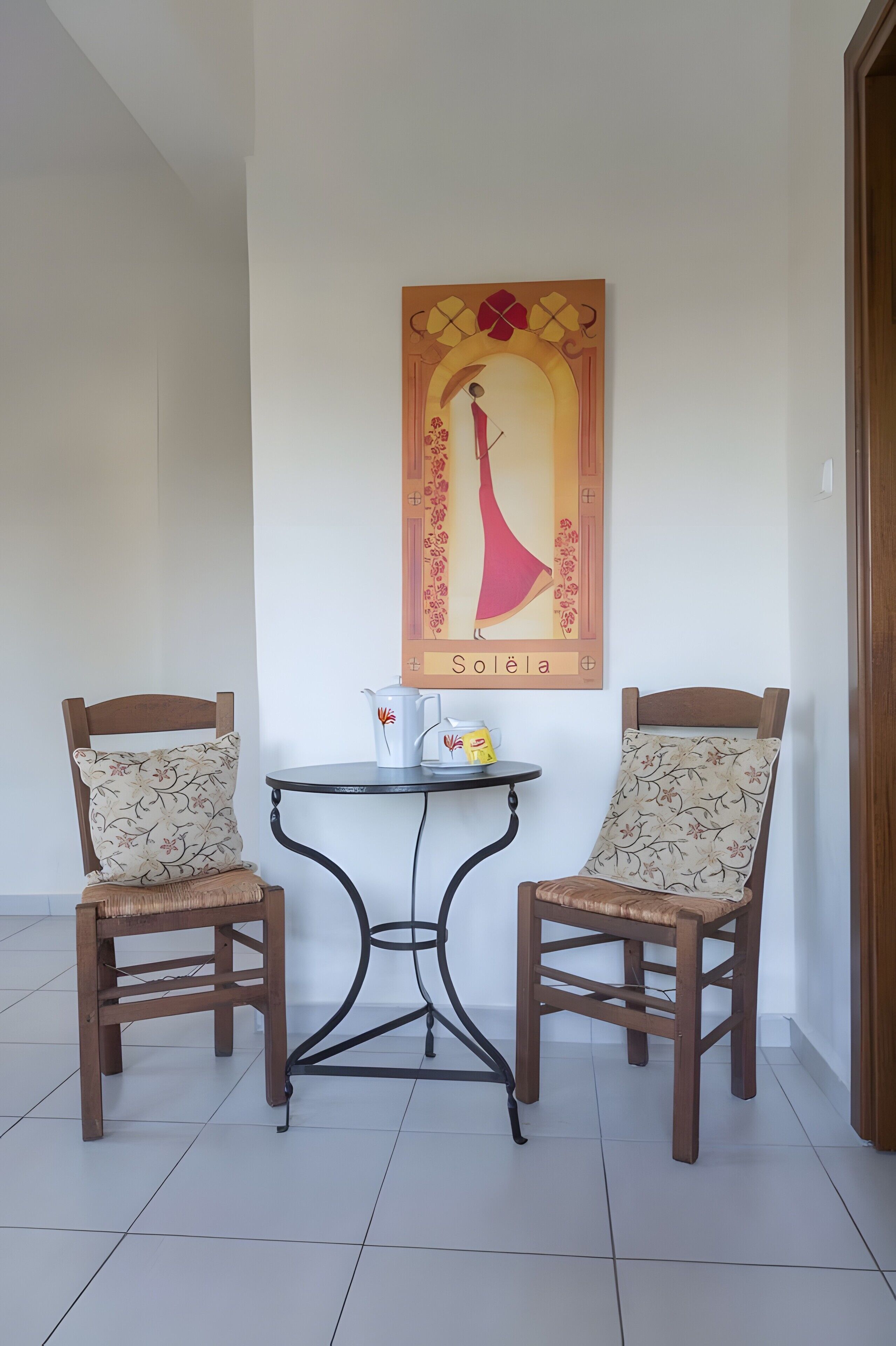 A room with two wooden chairs, a small round table, and a wall-mounted artwork depicting a giraffe.