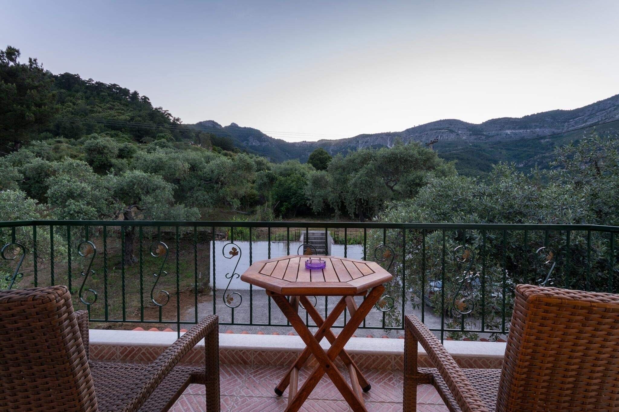 Ein Balkon mit Korbmöbeln, einem Tisch und Blick auf eine Berglandschaft.