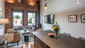 Una sala de estar moderna con pared de ladrillo, ventanas amplias, chimenea, zona de comedor y televisor de pantalla plana.