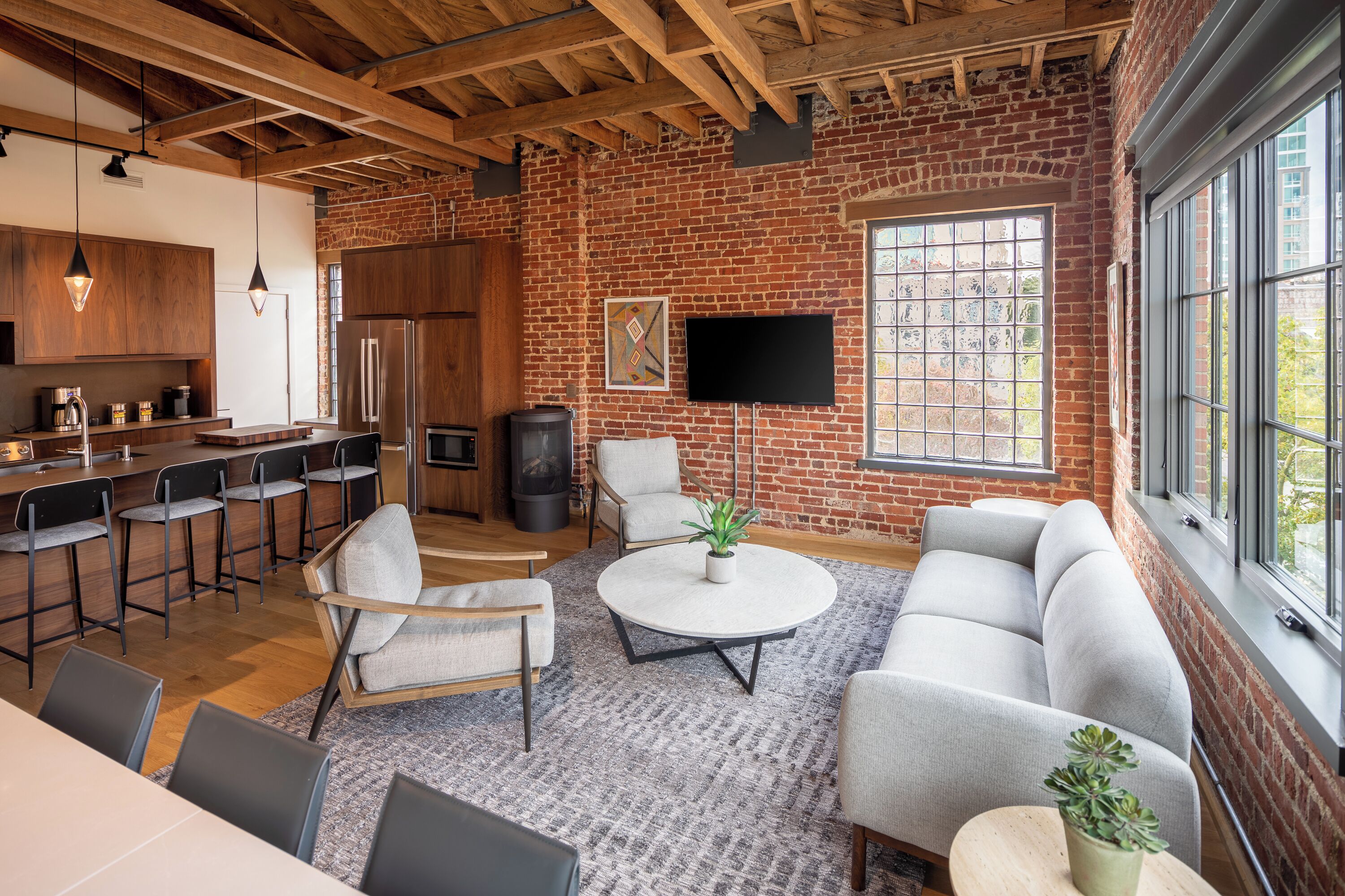 A modern kitchen with a brick wall, a flat-screen TV, and a dining area with a round coffee table.