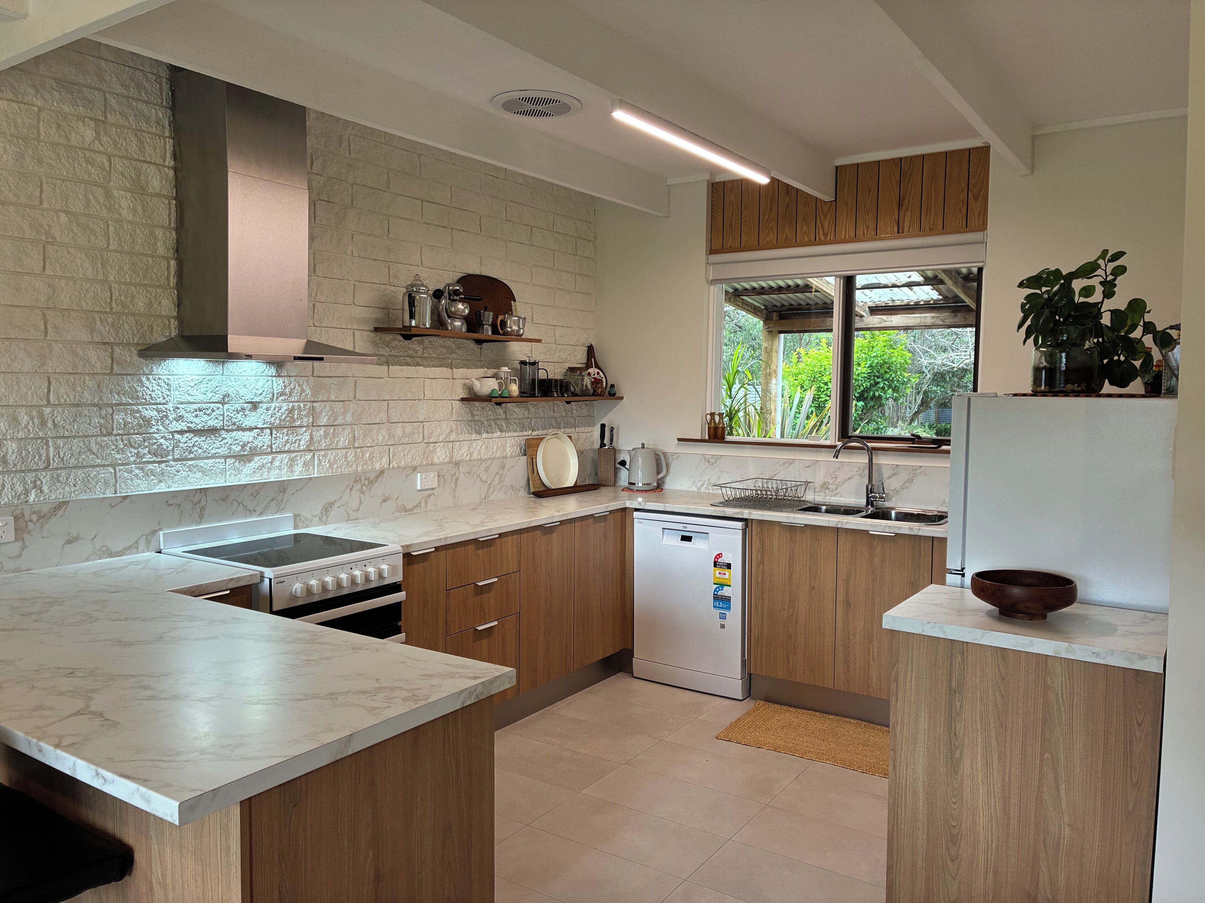 Een moderne keuken met marmeren aanrechtbladen, houten keukenkastjes en een ingebouwde vaatwasser.