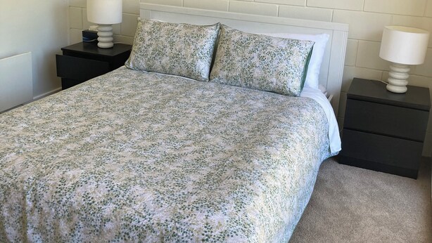 A bedroom with a bed, two nightstands, a wall-mounted painting, and a white brick wall.