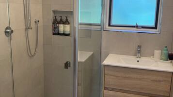 A modern bathroom with a glass-enclosed shower, a sink with a mirror above, and toiletries on the wall.