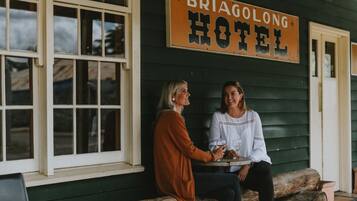 Zwei Personen sitzen an einem Tisch vor einem Gebäude, an dem ein Schild mit der Aufschrift 'BRIAGOLONG HOTEL' hängt.