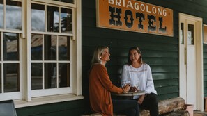 Two people sitting at a table outside a building with a sign that reads 'BRIAGOLONG HOTEL'.