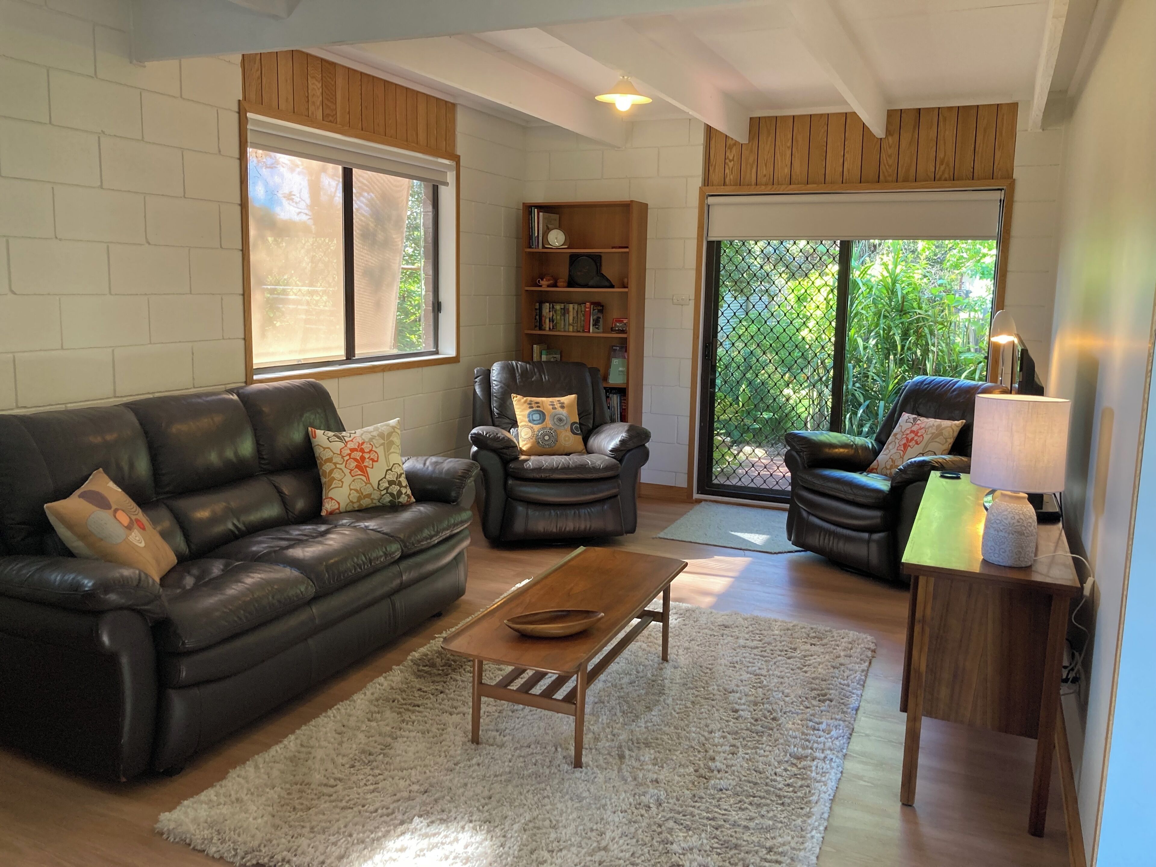 A living room with a leather sofa, armchairs, a coffee table, and a bookshelf.