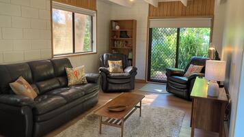 A living room with a leather sofa, armchairs, a coffee table, and a bookshelf.