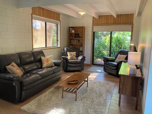 A living room with a leather sofa, armchairs, a coffee table, and a bookshelf. - Cosy mid-century cottage in Briagolong. (Briagolong)