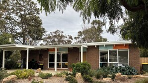 A modern house with a covered patio, large windows, and a well-maintained garden with various plants and flowers.