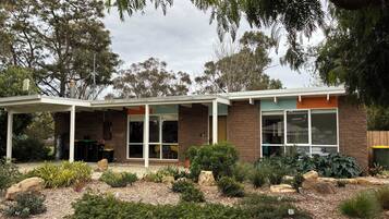 A modern house with a covered patio, large windows, and a well-maintained garden with various plants and flowers.