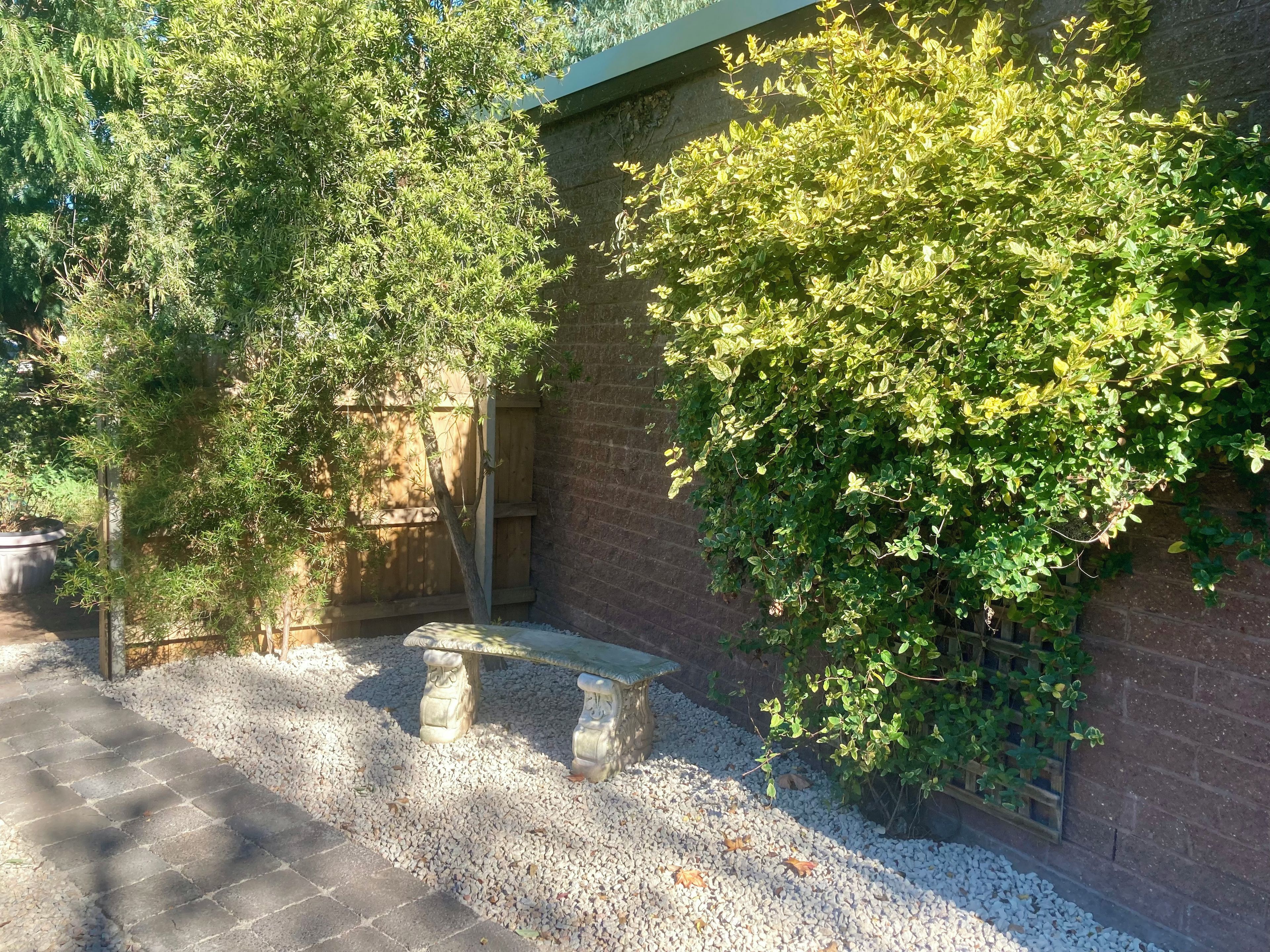 Une cour avec un banc en pierre, un sol recouvert de gravier et un mur de briques orné de plantes grimpantes.