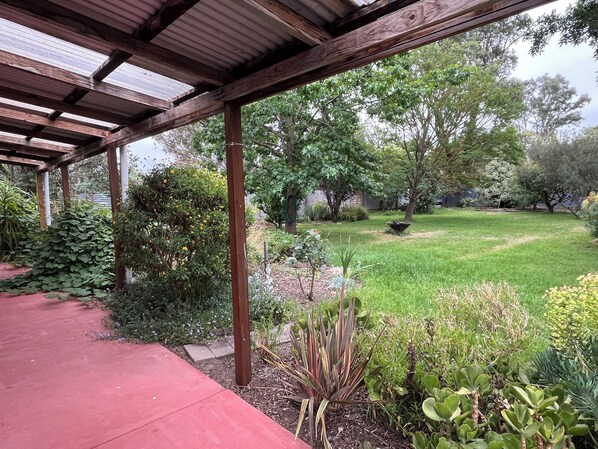 A covered outdoor area with a red pathway, surrounded by various plants and trees.