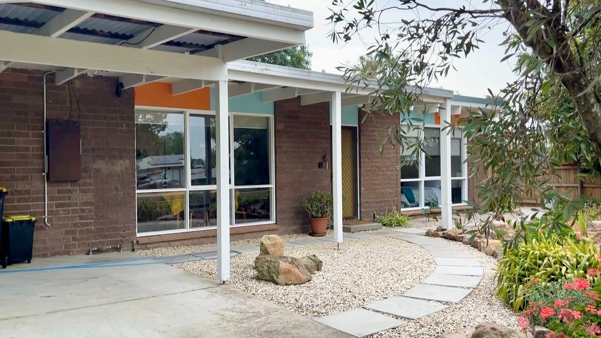 A modern house with a covered patio, large windows, and a garden with gravel and plants.