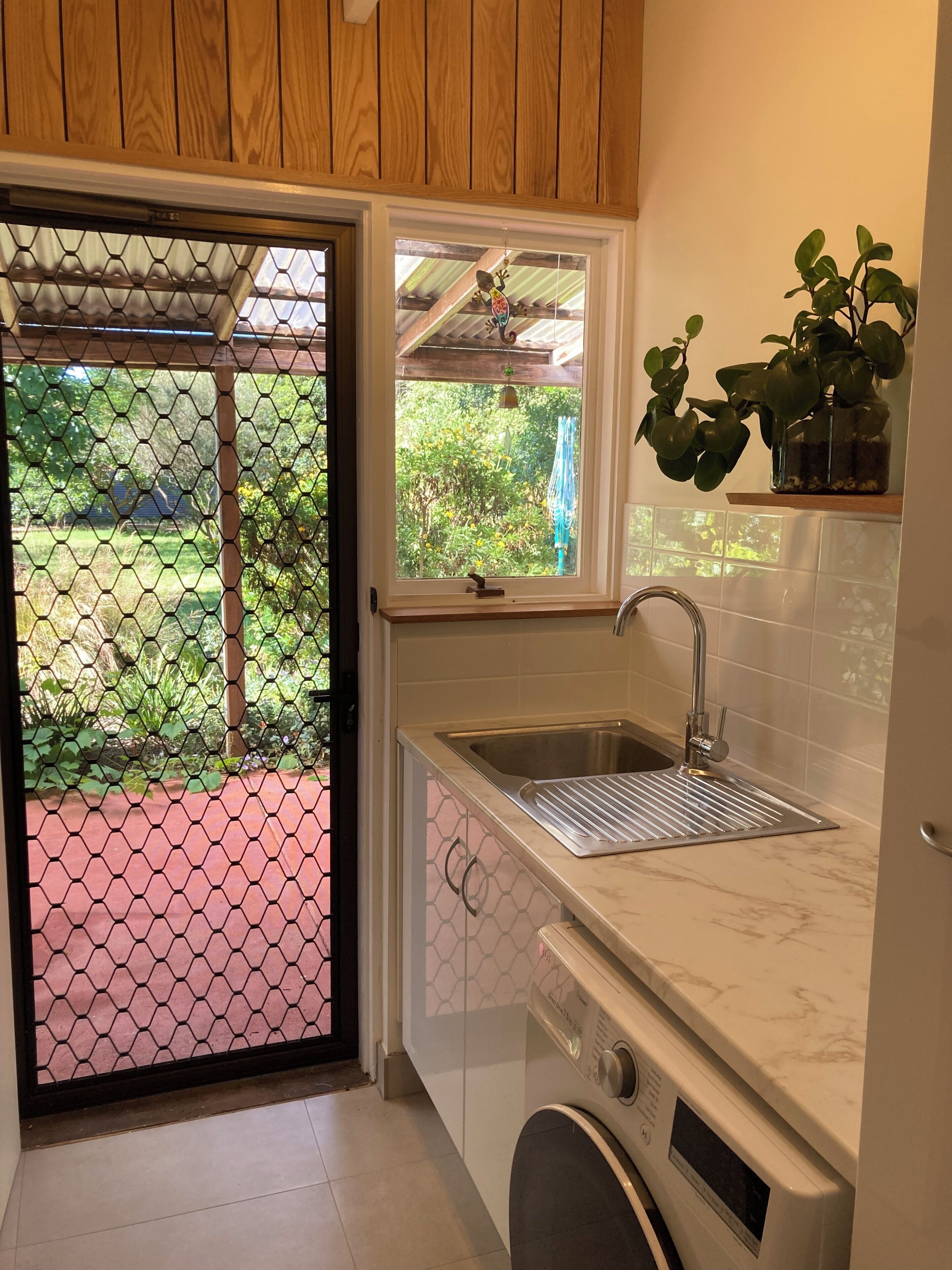 A kitchen with a built-in washing machine, a sink, and a window overlooking a garden.