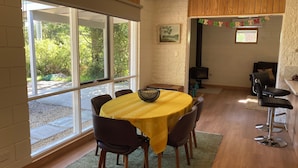 A dining area with a round table, chairs, and a view through large windows.