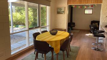 A dining area with a round table, chairs, and a view through large windows.