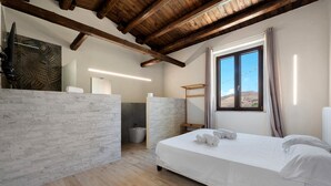 Una camera da letto con soffitto in legno, un'ampia finestra vista, un letto con lenzuola bianche e un bagno dal design moderno.