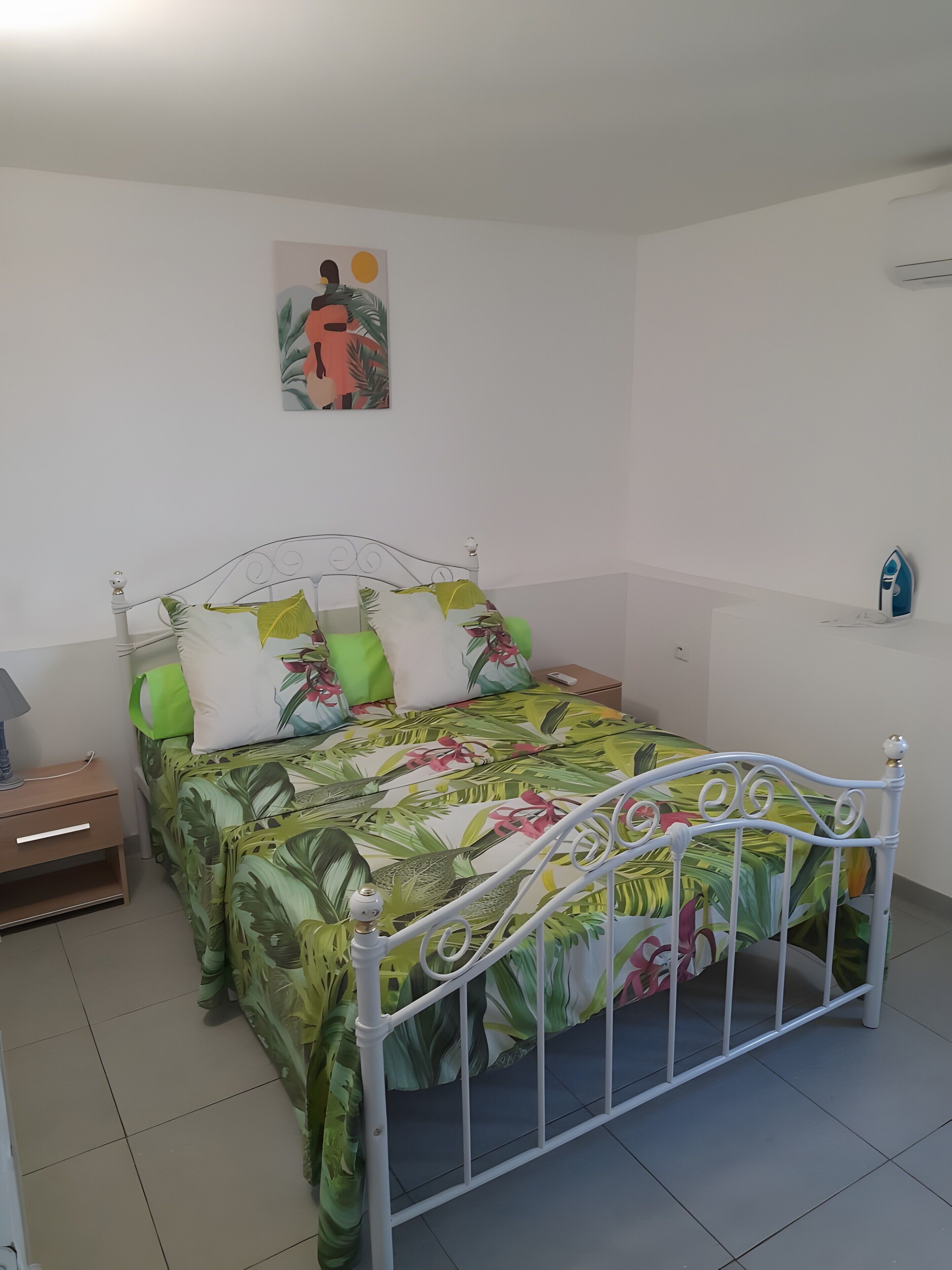 A bed with a metal frame, a nightstand with a lamp, and a wall-mounted air conditioner.