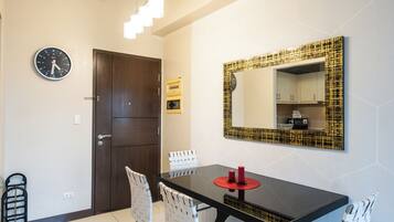 A modern dining area with a black table, white chairs, a wall clock, and a decorative mirror.