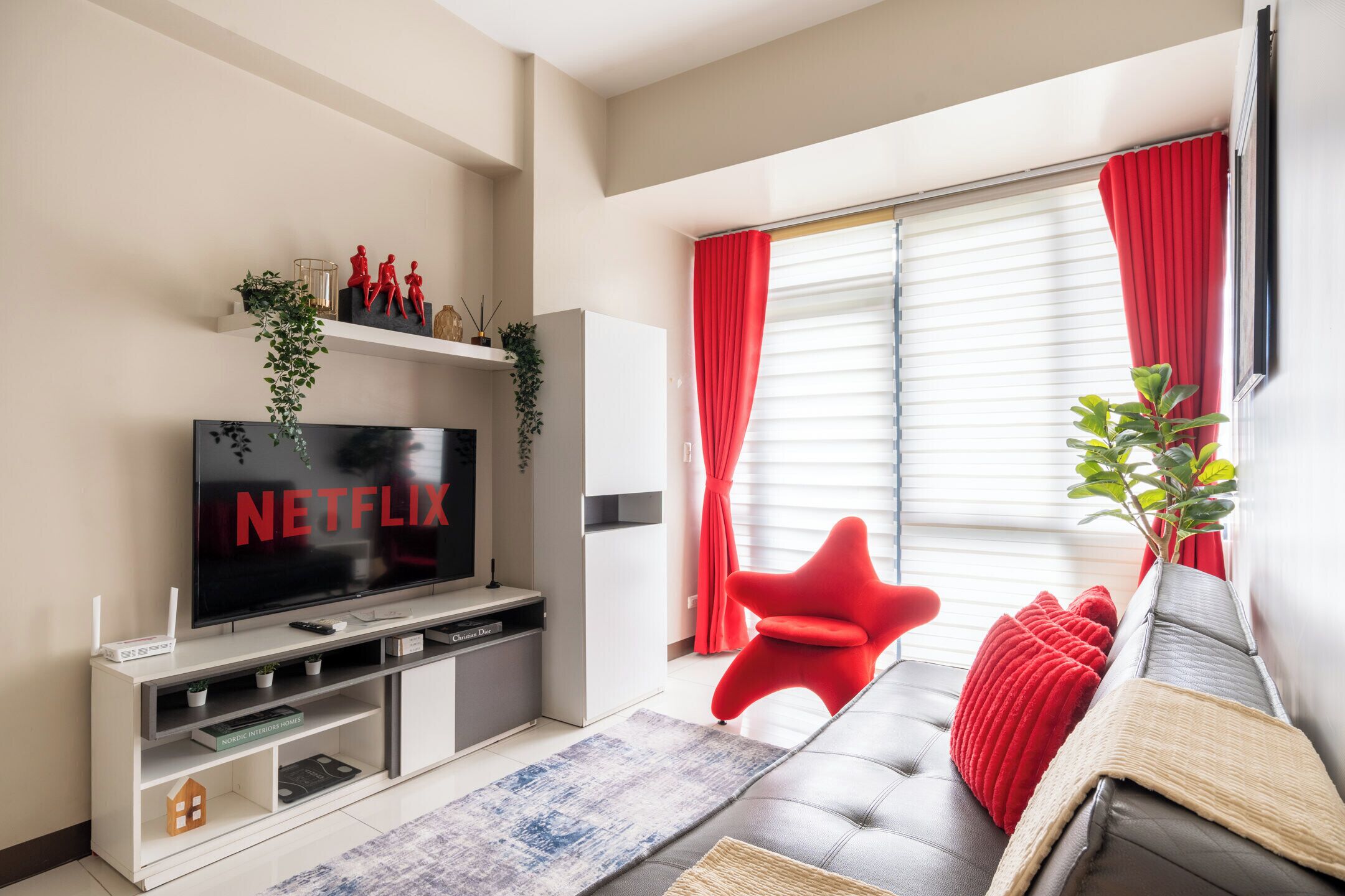 A modern living room with a flat-screen TV, a red chair, and a sofa with red cushions.