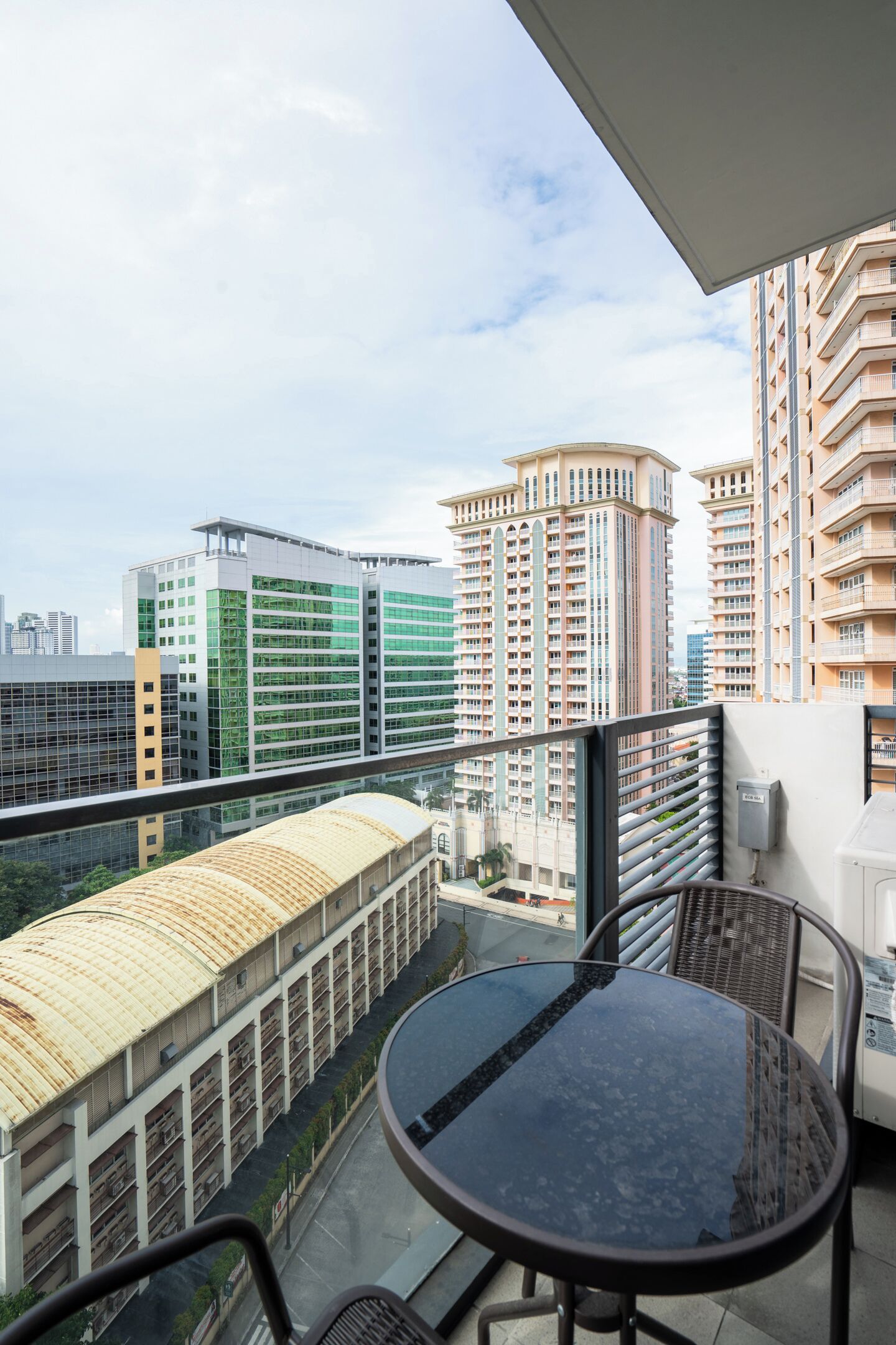 A balcony with a glass table and chairs, overlooking a cityscape with modern buildings.